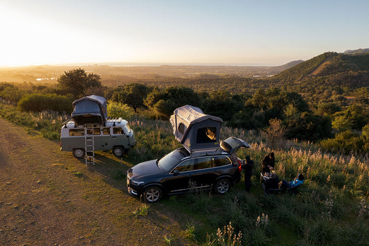 image of two cars with roof top tents set up in a field with a natural landscape at sunset.