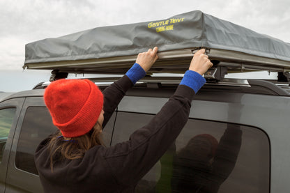 A woman packing up the SKY LOFT rooftop tent and securing it on the roof rack for the drive home.