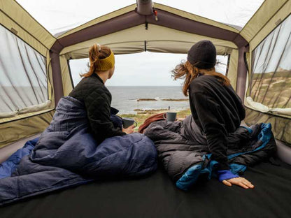 Two campers in their sleeping bags enjoying the view of the ocean from the GT SKY LOFT rooftop tent
